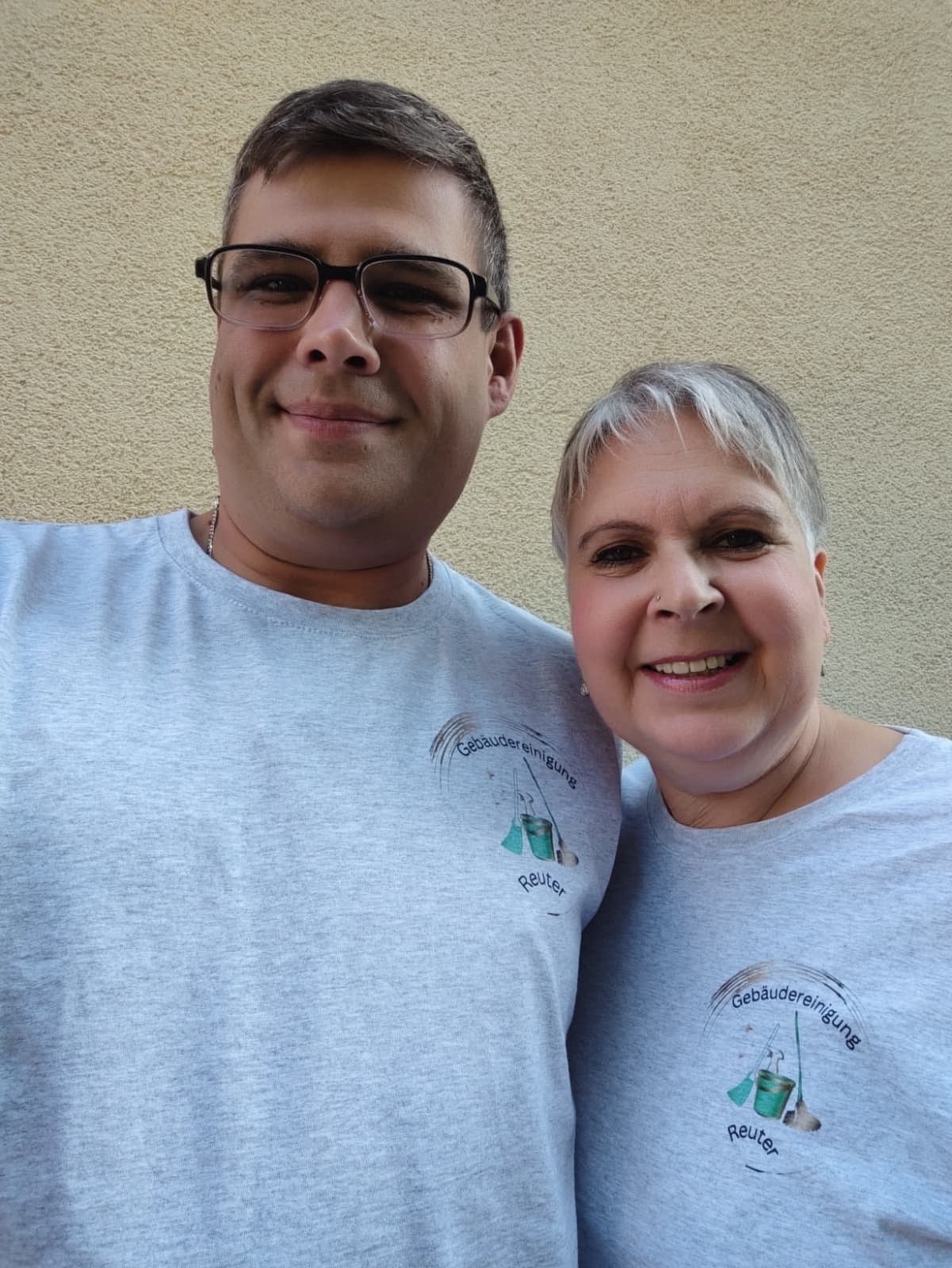 Zwei Personen vom Team Gebäudereinigung Reuter, lächelnd, in grauen T-Shirts mit dem Firmenlogo